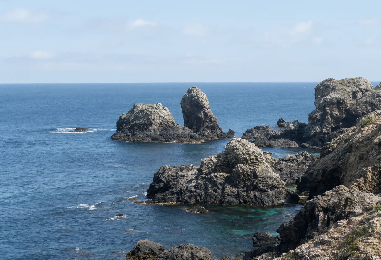 Large rocky formations along a blue ocean coastline beneath a bright blue sky. (AI-generated)
