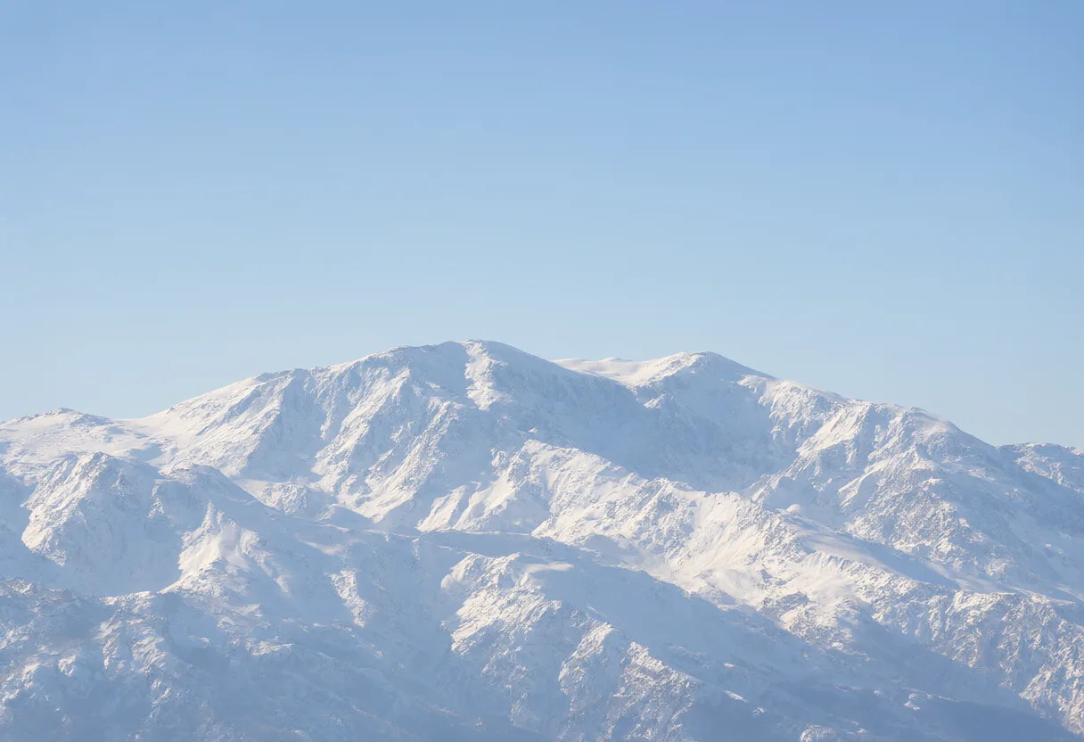 Wide panorama of snow-covered mountain peaks beneath a clear blue sky. (AI-generated)