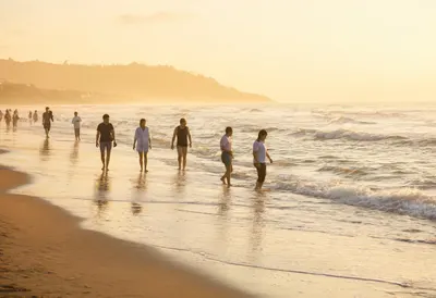 ผู้คนกำลังเดินเลียบชายหาดท่ามกลางแสงพระอาทิตย์ตกสีทองอันอบอุ่น